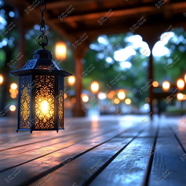 An image of an ornate metal lantern hanging from above, illuminated by an internal candle emitting a warm glow. The lantern is suspended over a wooden floor, with several other blurred lights in the background, creating a serene and beautiful ambiance in an outdoor nighttime setting.