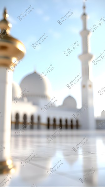 Image of a mosque with elegant white architecture, featuring a large white dome and a tall minaret. In the foreground, there is a pillar decorated with gold, while the mosque with its arches and windows extends into the background under a clear blue sky.