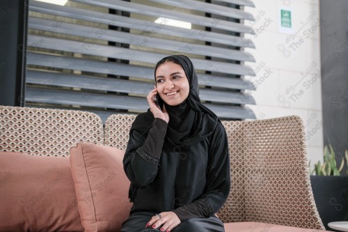 A Saudi woman wearing an abaya holds a mobile phone and displays its screen