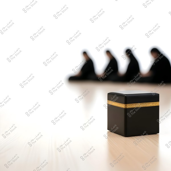The image shows a cube resembling the Kaaba in black with a golden band, positioned in the foreground. In the background, there are four individuals sitting in a row and bowing, indicating they are in a prayer position. The image conveys a sense of calmness and spirituality.