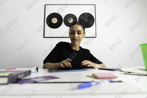 امرأة تجلس عند مكتب تتعامل مع جهاز لوحي, وخلفها لوحة تحتوي على ثلاث إسطوانات فينيل معلقة على الحائط.