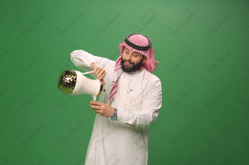 شاب سعودي على خلفية خضراء يرتدي الثوب و الشماغ، يقوم بعمل حركات بيده، يصب القهوه السعودية، احتفالات العيد