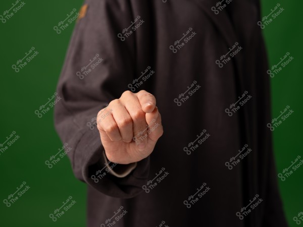 يد شخص مرتدية ملابس داكنة تشير إلى الأمام مع خلفية خضراء.