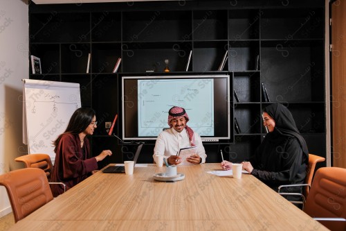 A Saudi man in traditional Saudi dress holds a meeting with Saudi female employees wearing abaya in the meeting room