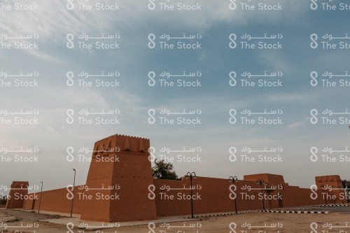 A heritage building in Dawadmi Governorate, in front of it is a group of lamps, and the sky appears almost clear during the day