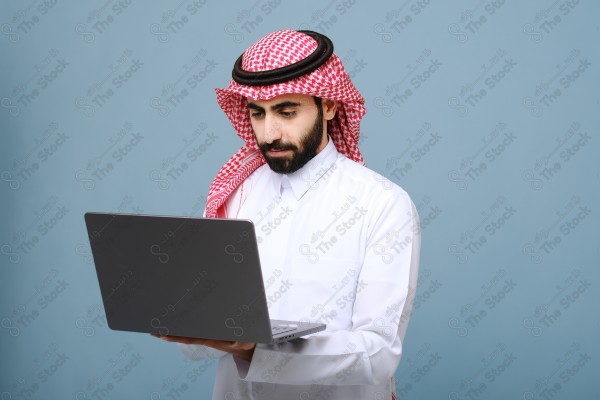 بورتريه شاب سعودي يرتدي الزي السعودي ينظر إلى جهاز المحمول ، يقف على خلفية سماوية