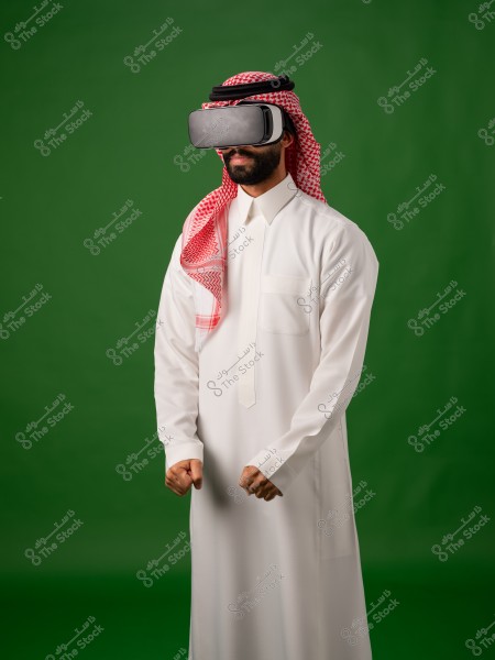 شخص يرتدي الزي التقليدي السعودي ونظارات الواقع الافتراضي أمام خلفية خضراء.