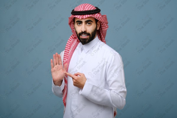 بورتريه شاب سعودي يرتدي الزي السعودي يقوم بالتفاعل بيدية ، ويظهر بتعابير وجه، على خلفية سماويه