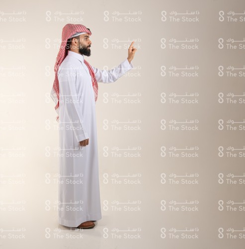 رجل سعودي يرتدي الزي السعودي التقليدي يشير بإصبعه السبابة للأعلى، رجل ينقر على أيقونة افتراضية