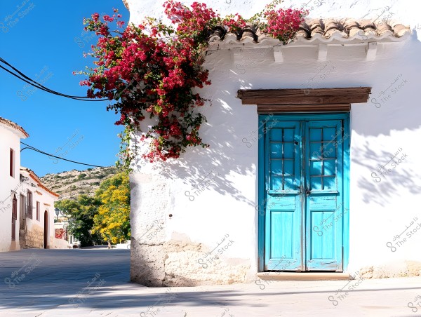 A building on a quiet street with a bright blue wooden door, adorned with red climbing flowers extending across the white wall. The building\'s roof features traditional details, and the clear blue sky and green trees are visible in the background.