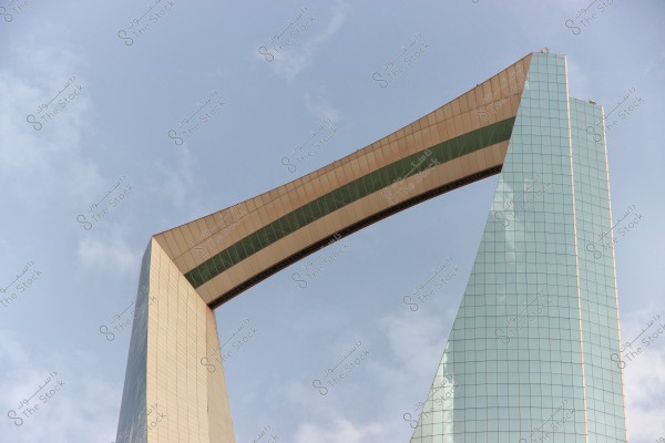 Image of a modern architectural building with a design resembling an arch at the top. The building features glass facades reflecting the blue sky and metallic structural elements. The background shows a clear sky with a few light clouds.