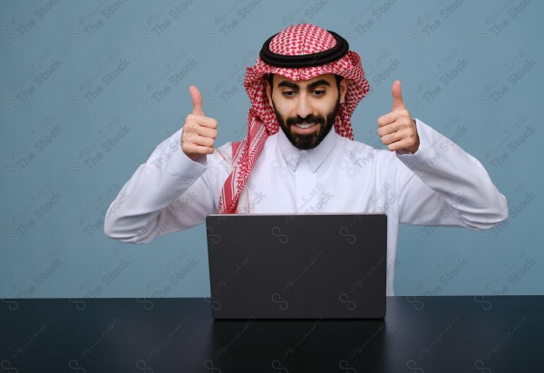 بورتريه شاب سعودي يرتدي الزي السعودي يستخدم جهاز المحمول ويتفاعل معه ، يقف على خلفية سماوية.