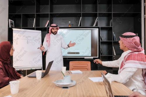 A Saudi man in traditional Saudi dress conducts a business meeting in the boardroom during the day