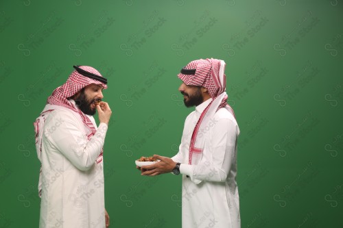 رجل سعودي يرتدي الزي السعودي التقليدي يقدم طبق من التمر لضيفه في أحد المناسبات