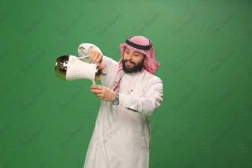 شاب سعودي على خلفية خضراء يرتدي الثوب و الشماغ، يقوم بعمل حركات بيده، يصب القهوه السعودية، احتفالات العيد