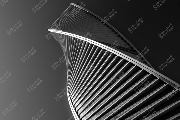 An image of a skyscraper with a twisted and modern design shown in black and white. The building features intersecting horizontal and vertical lines and is positioned in the lower corner of the image, fading as it rises upward. The surrounding sky is a dark gray color.