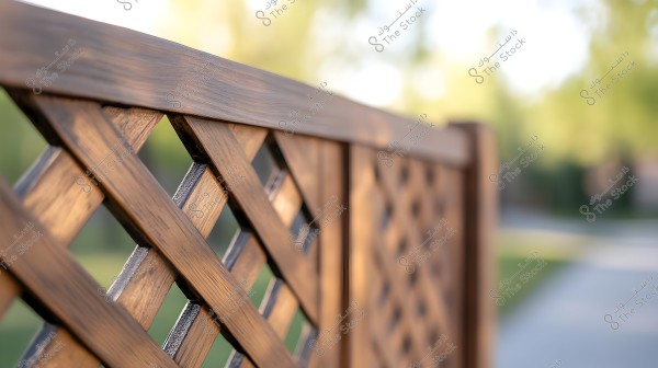 A close-up image of a section of a wooden fence with a lattice design. The wooden panels are arranged in a crisscross pattern with a natural brown finish. The background is blurred, showcasing soft hues of nature with shades of green and muted yellow.