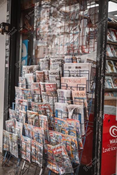 A collection of magazines and newspapers displayed for sale at a wooden kiosk.