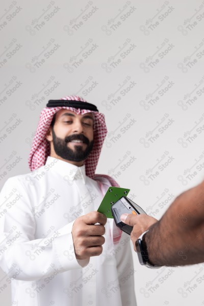 Portrait of a Saudi man holding a card and making automatic payments on a white background