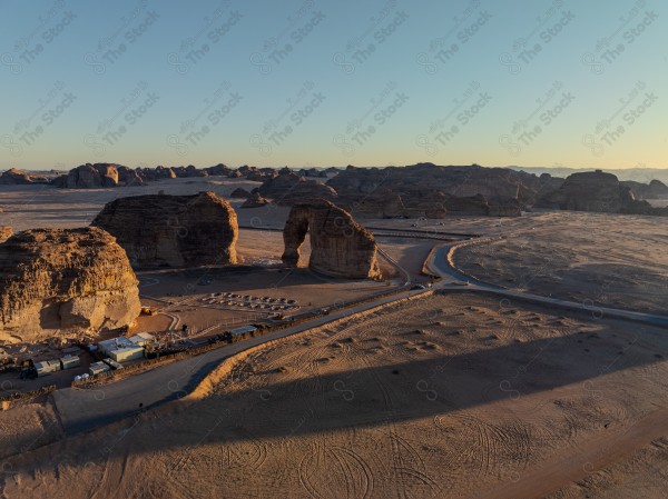 Aerial view of rock formations in a vast desert area, with mountains in the background and tracks on the sand.