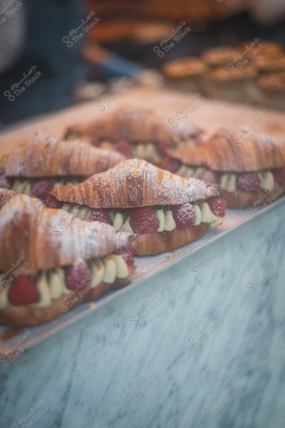 Croissants filled with cream and red raspberries placed on a marble table.