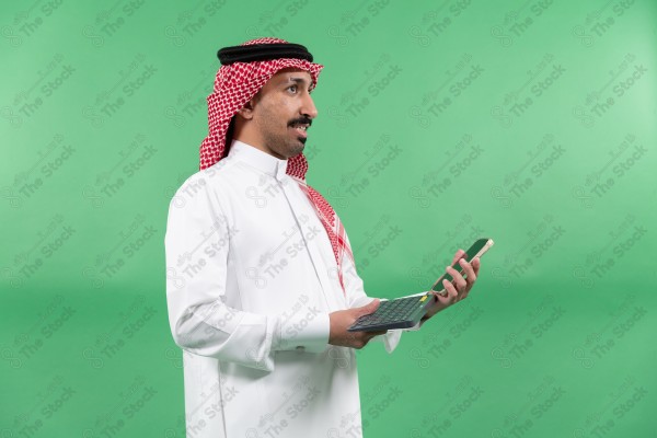 رجل "من ذوي الاعاقة" يرتدي الزي السعودي التقليدي يمسك هاتفاً محمولاً ولوحة مفاتيح، وخلفه خلفية خضراء.