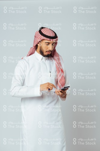 بورتريه رجل سعودي يرتدي الزي السعودي التقليدي يستخدم الجوال وينظر للشاشة بينما يتصفحه