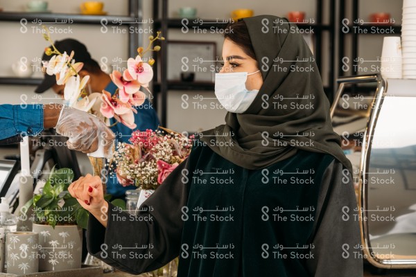 A Saudi girl wears an abaya and a mask in a café whose temperature is measured as part of the Corona precautionary measures