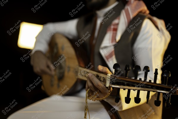 A person playing the oud, wearing traditional attire, with a dark background.
