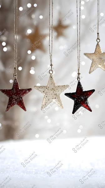 An image of four star ornaments hanging by strings. The stars are made of a glittery material, with colors ranging from dark red to white. The background is blurred with small white lights resembling snow or sparkling lights, creating a festive atmosphere.