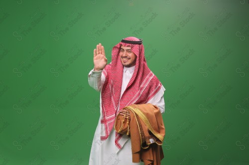 Portrait of a smiling Saudi man in traditional Saudi dress holding a bisht over his arm and pointing palms forward, a smiling Saudi man in Saudi dress holding a bisht and saluting