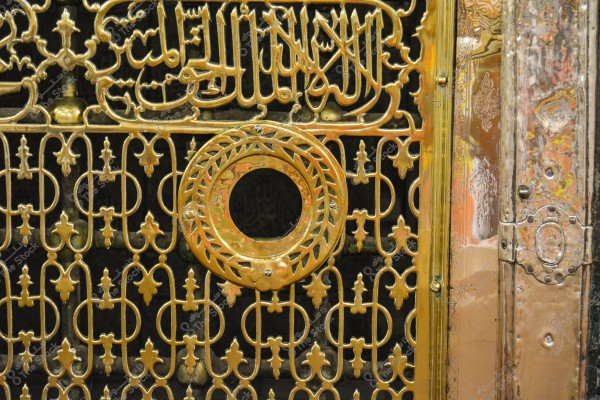 A portion of a golden metallic design featuring Arabic inscriptions and ornate patterns. The design is intricate with a circle in the center, showcasing geometric engravings and detailed craftsmanship. It appears to be part of Islamic architectural work.