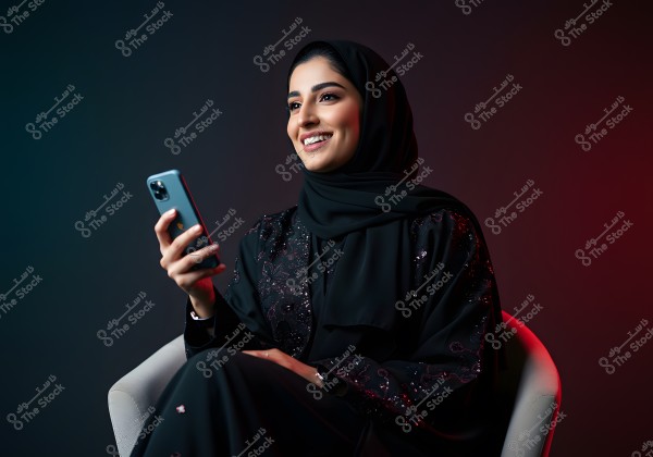 Portrait of a woman wearing an embellished black abaya and hijab, sitting on a white chair while holding a smartphone. She is smiling gently against a background with dark and red hues.