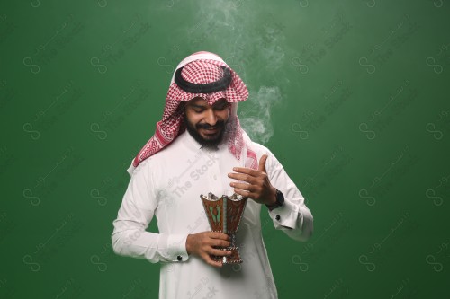 بورتريه رجل سعودي يرتدي الزي السعودي التقليدي يحمل المبخرة ويتطيب بالبخور