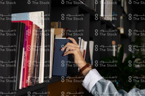 فتاة سعودية ترتدي العباءة تقف أمام المكتبة بينما تختار كتابًا من المكتبة