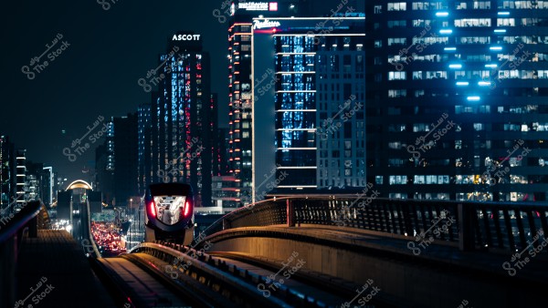 A train traveling on a track in a city illuminated by building lights at night.