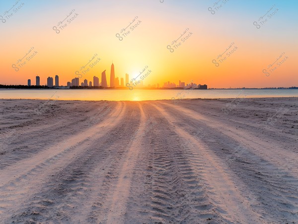 A sunset view over a modern city skyline with several skyscrapers. The foreground shows sandy tracks from vehicle tires leading to calm waters. The sky is filled with shades of orange and blue during the sunset.