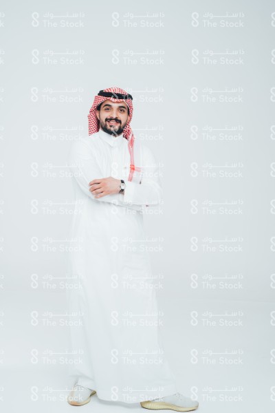 بورتريه رجل سعودي يرتدي الثوب ويقف أمام خلفية بيضاء، يتفاعل بحركات تعبيرية بيديه