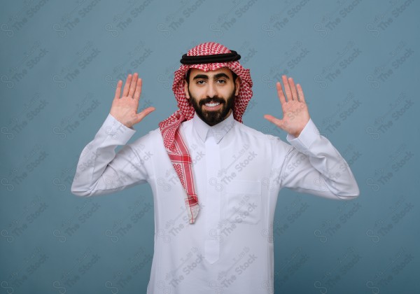 بورتريه شاب سعودي يرتدي الزي السعودي يقوم بالتفاعل بيدية ، ويظهر بتعابير وجه، على خلفية سماويه