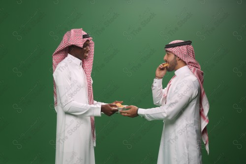 رجل سعودي يرتدي الزي السعودي التقليدي يقدم لضيفه طبق المعمول في إحدى المناسبات