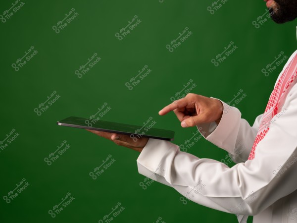 رجل يرتدي ثوبًا سعوديًا تقليديًا يستخدم حاسوبًا لوحيًا أمام خلفية خضراء.