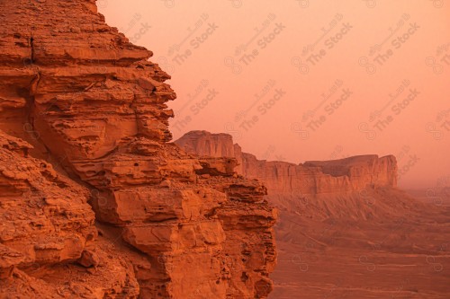 A group of people standing at the edge of the world at sunset, of the Tuwaiq mountain range in the Najd region