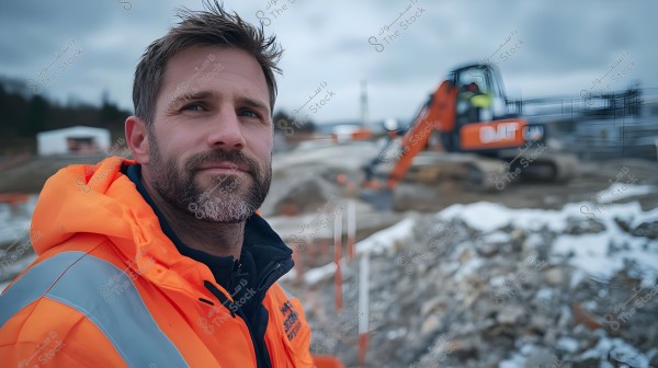 Image of a man wearing an orange reflective jacket standing at a construction site. In the background, there is an excavator with another worker operating it. The site is partly covered in snow under a cloudy sky.