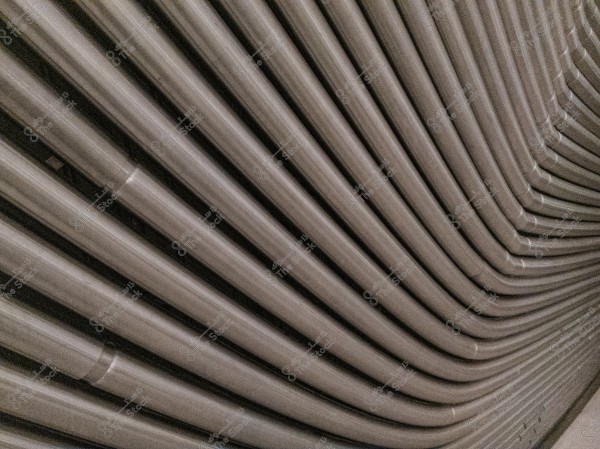 An image showing a set of gray metallic pipes arranged in a parallel and curved manner, forming a repeating pattern. The smooth texture and slight shine give it an industrial and uniform appearance.