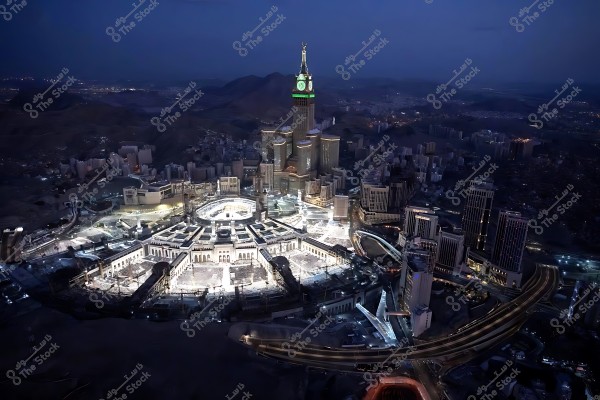 Aerial view of the Kaaba in the Grand Mosque in Mecca at night, with the Clock Tower prominently visible in the background.