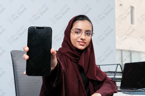 A Saudi woman wearing an abaya holds a mobile phone and displays its screen