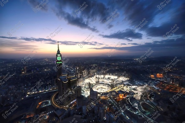 Aerial view of Mecca at sunset, with the Clock Tower and the illuminated Grand Mosque, city lights in the background.