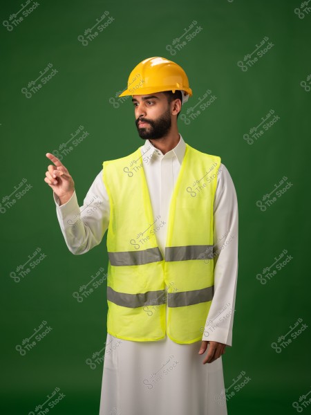 شخص يرتدي خوذة سلامة صفراء وسترة عاكسة صفراء على خلفية خضراء ويشير بإصبعه.