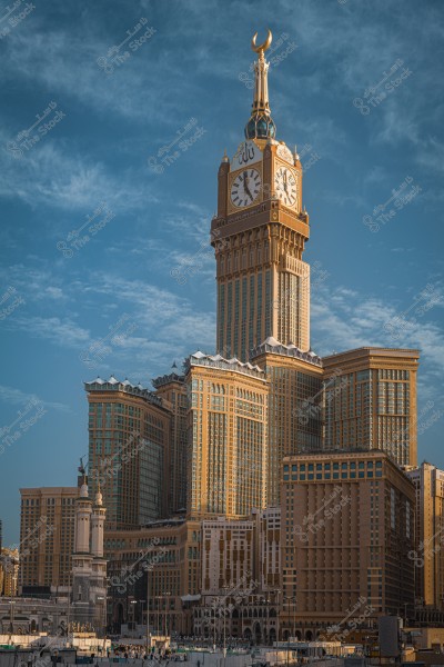 Image of the Makkah Clock Tower, also known as the Abraj Al Bait Tower in Mecca, Saudi Arabia. The massive tower features its golden facade with a large clock at the top and the surrounding view. The blue sky is visible in the background.
