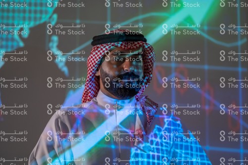 رجل سعودي يرتدي الزي السعودي التقليدي يتابع سوق الأسهم بينما تنعكس أضواء الشاشة عليه